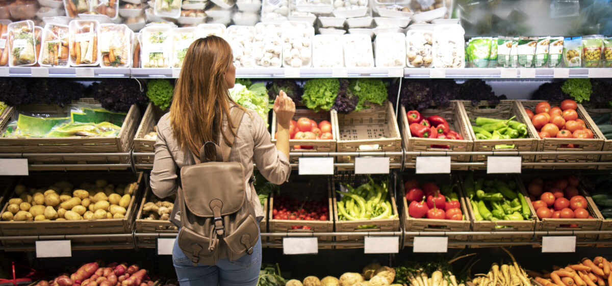 Good looking woman standing in front of vegetable shelves choosing what to buy.
